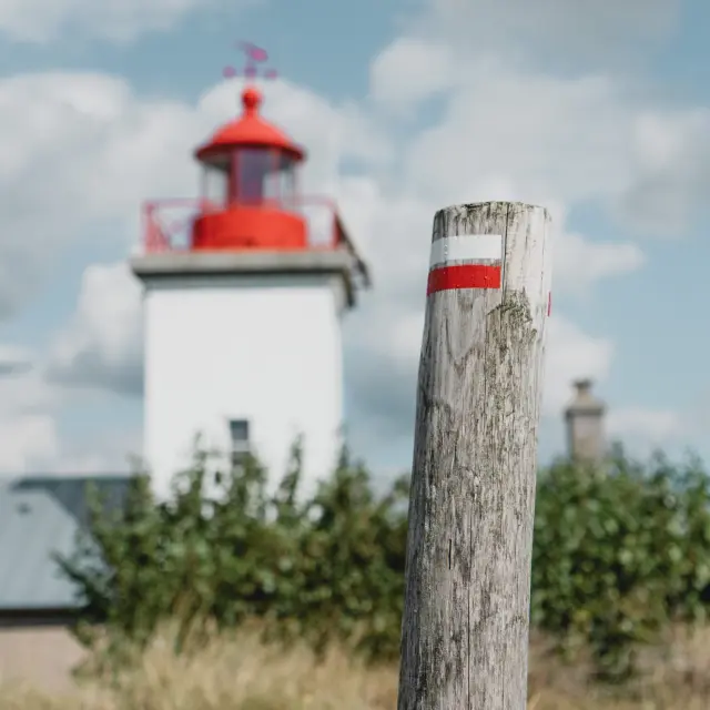 White lighthouse with a red roof and a wooden post marked with red and white stripes