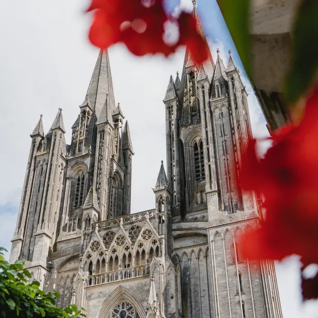 Deux tours pointues de la cathédrale gothique de Coutances avec des fleurs rouges en premier plan