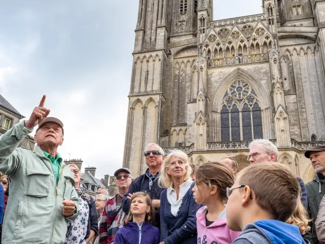 Un groupe de personnes écoutant un guide devant la cathédrale de Coutances