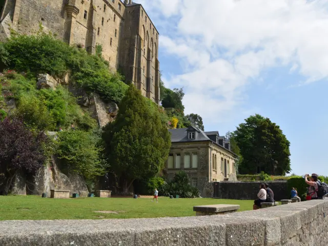 Medieval castle perched on a cliff with trees and people resting on the grass