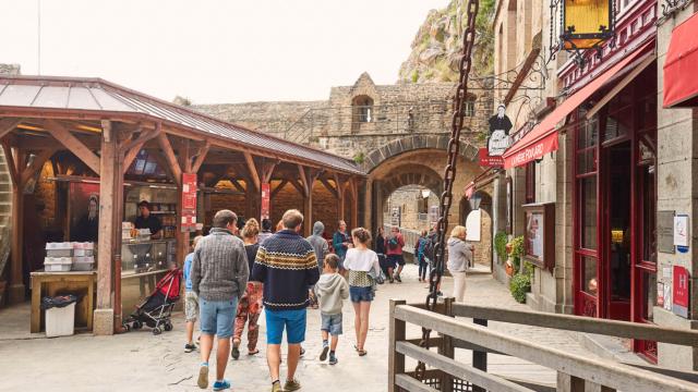 Personnes marchant dans une rue commerçante avec des boutiques et des stands au Mont-Saint-Michel