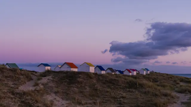 A row of colorful beach huts on a dune at sunset