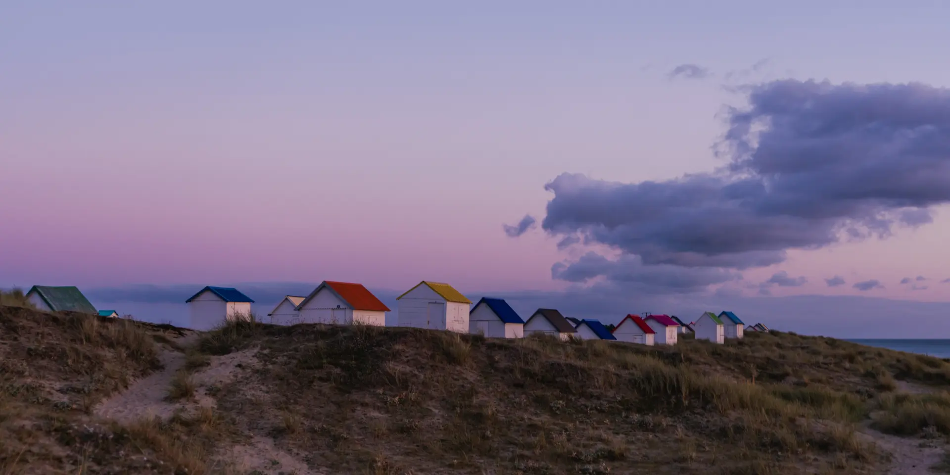 A row of colorful beach huts on a dune at sunset