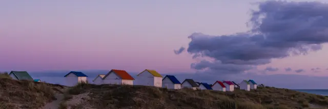 Eine Reihe bunter Strandhütten auf einer Düne beim Sonnenuntergang