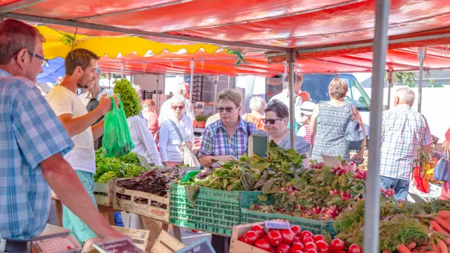 Personnes faisant leurs courses dans un marché sous des tentes rouges et jaunes à Hauteville Sur Mer