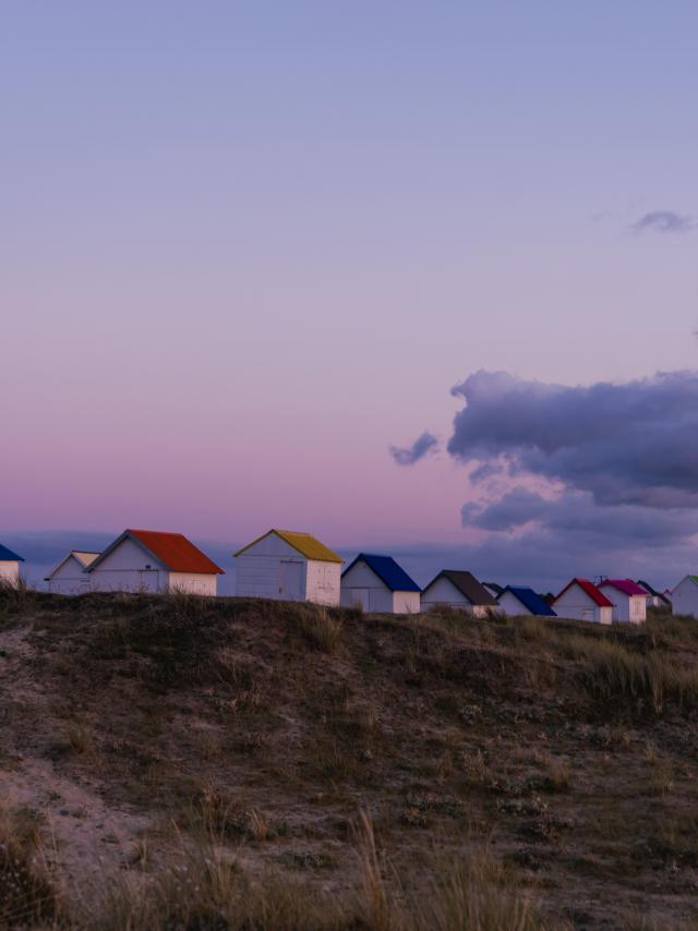 A row of colorful beach huts on a dune at sunset