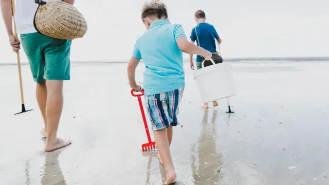 Trois enfants marchent sur la plage avec des seaux et des pelles pour aller à la pêche à pied à Agon-Coutainville