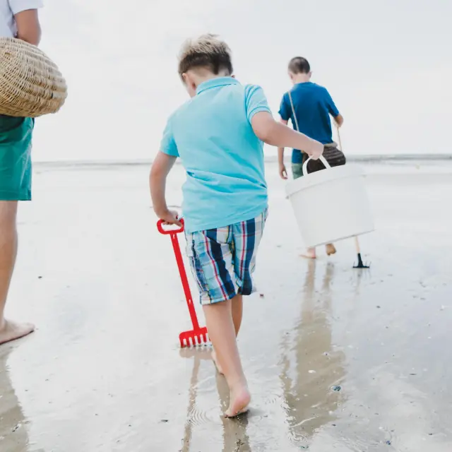 Trois enfants marchent sur la plage avec des seaux et des pelles pour aller à la pêche à pied à Agon-Coutainville