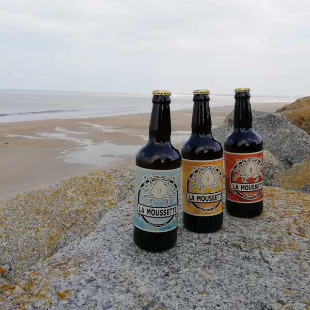 Trois bouteilles de bière La Moussette sur des rochers près de la plage
