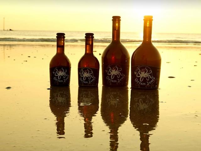 Quatre bouteilles de Captain James sur une plage au coucher du soleil
