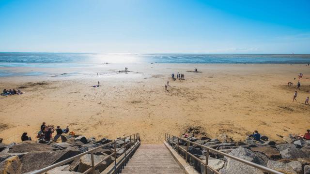 Escaliers menant à une plage de sable avec des gens se relaxant et jouant près de l'eau