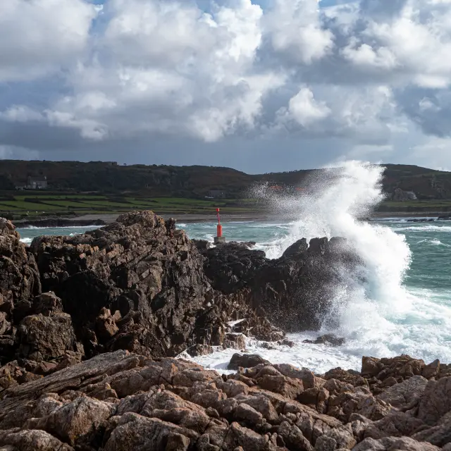 Waves crashing on rocks with a coastal landscape in the background