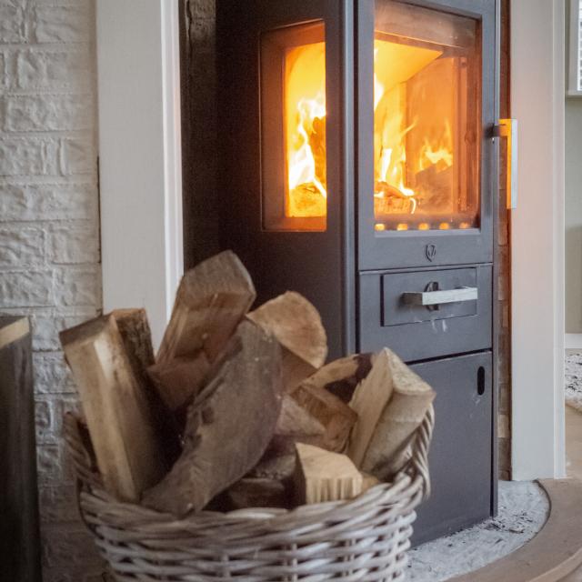 Wood stove with visible flames and a basket of wood next to it