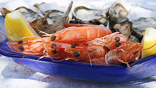 Fresh shrimp on a blue plate with lemons and shells in the background