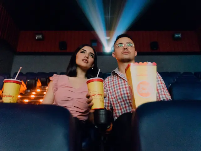 Un couple assis dans une salle de cinéma avec des boissons et du popcorn
