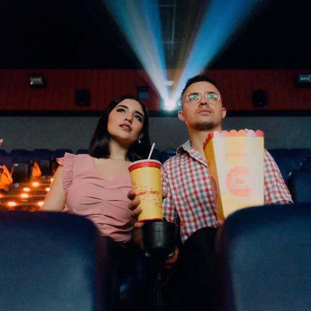 Un couple assis dans une salle de cinéma avec des boissons et du popcorn