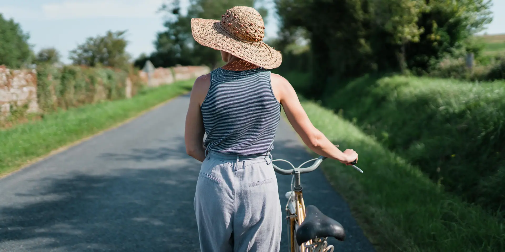 Une personne en vélo sur une route de campagne, portant un chapeau de paille et des vêtements légers
