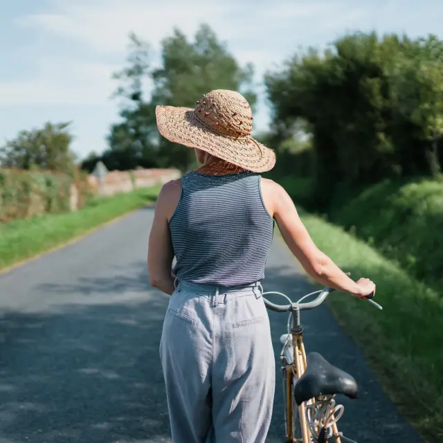 Une personne en vélo sur une route de campagne, portant un chapeau de paille et des vêtements légers