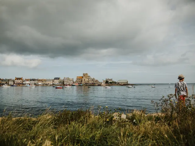 Person standing on a grassy hill overlooking a coastal village