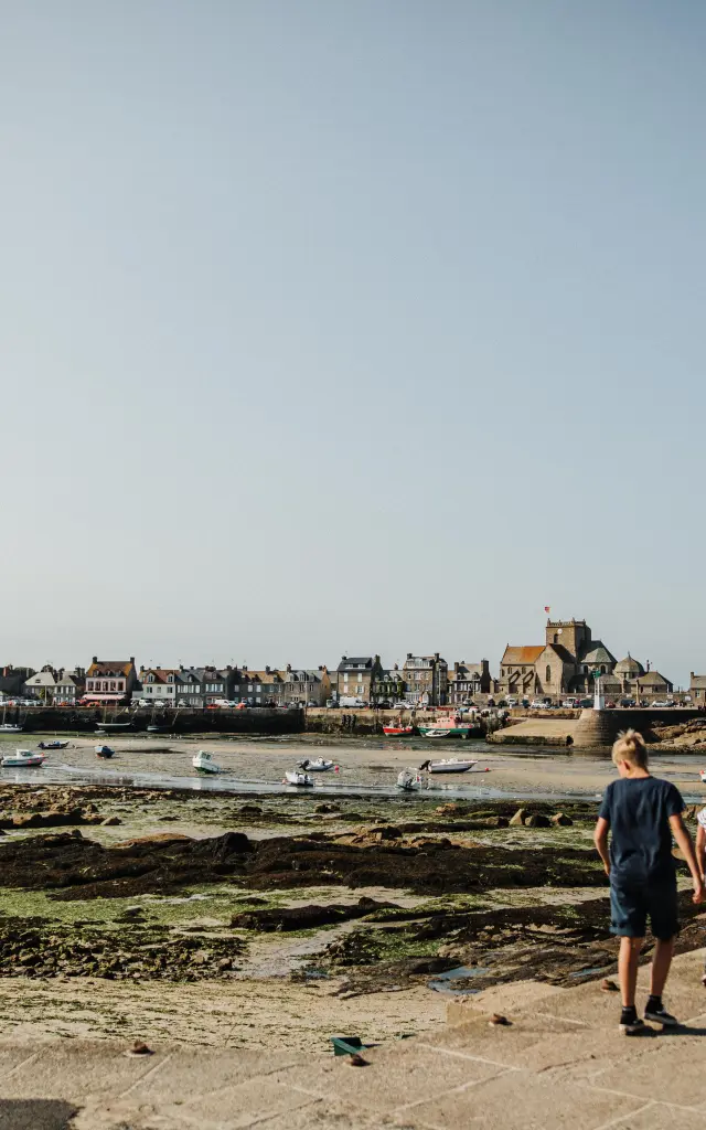 Two people walking on a seaside path with boats in the background