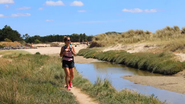 Une femme en randonnée sur un sentier près d'une plage avec des dunes de sable