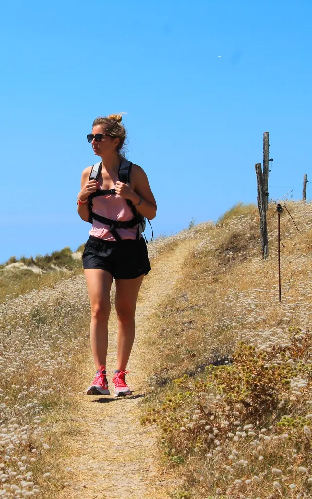 Une femme marche sur un sentier côtier avec la mer en arrière-plan - Randonnée