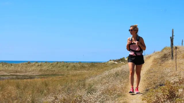 Une femme marche sur un sentier côtier avec la mer en arrière-plan - Randonnée