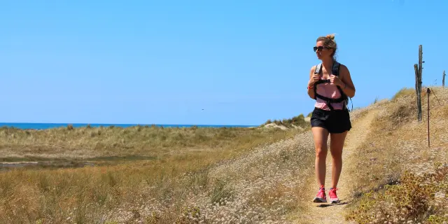 Une femme marche sur un sentier côtier avec la mer en arrière-plan - Randonnée