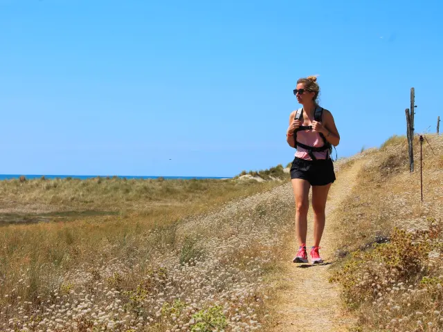 Une femme marche sur un sentier côtier avec la mer en arrière-plan - Randonnée