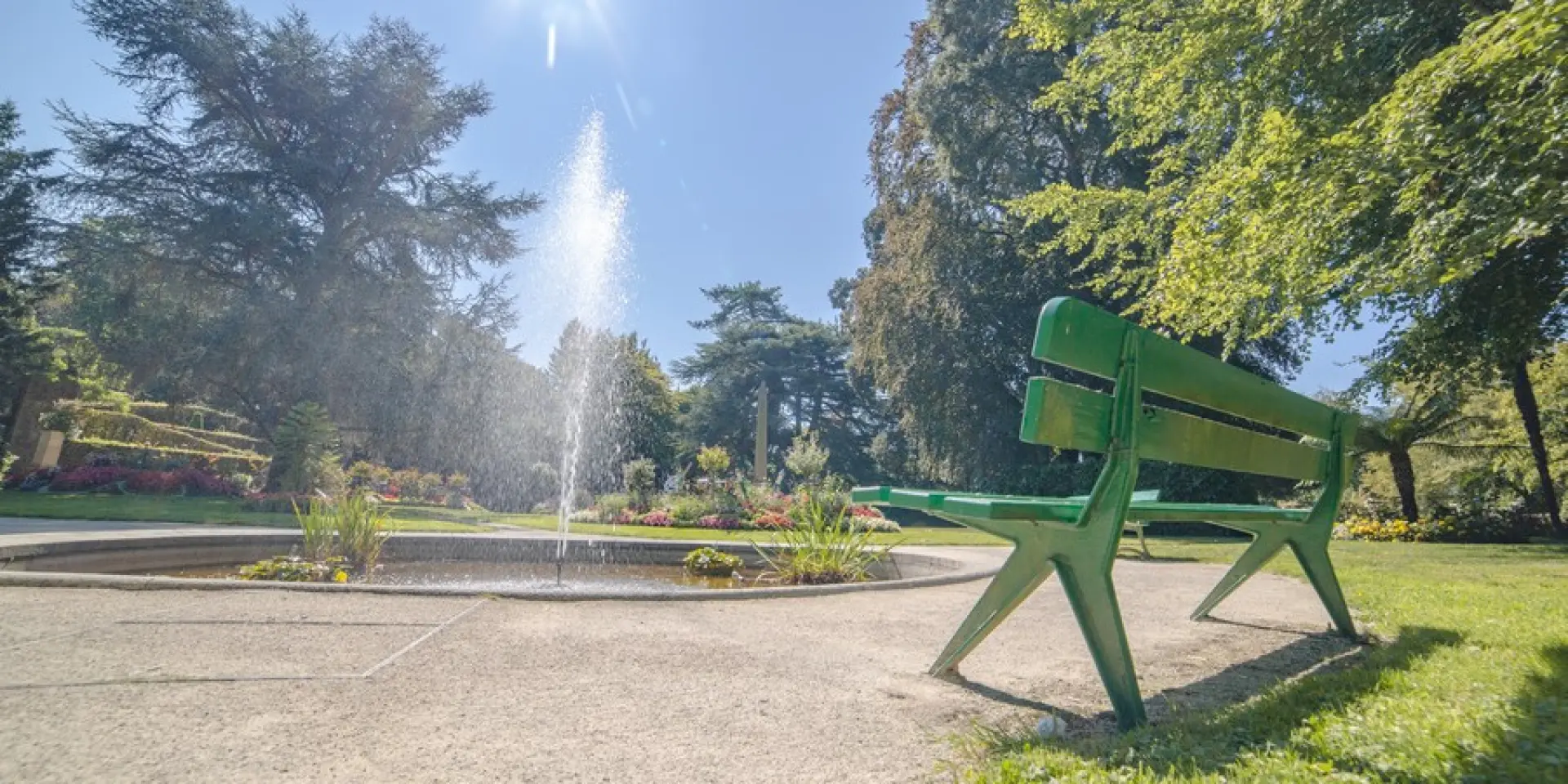 Un banc vert dans un jardin avec une fontaine au centre au jardin des plantes de Coutances