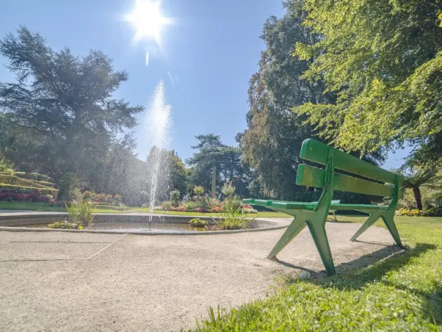 Un banc vert dans un jardin avec une fontaine au centre au jardin des plantes de Coutances