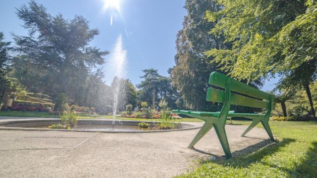 Un banc vert dans un jardin avec une fontaine au centre au jardin des plantes de Coutances