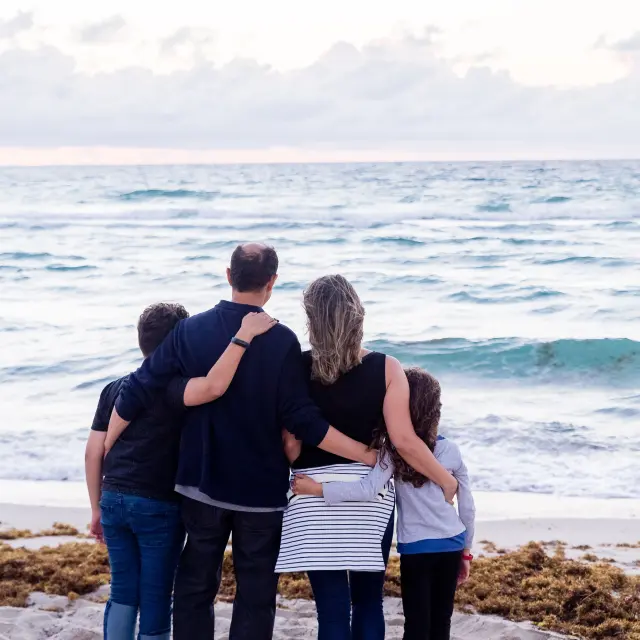 Une famille de quatre personnes se tient sur une plage face à l'océan
