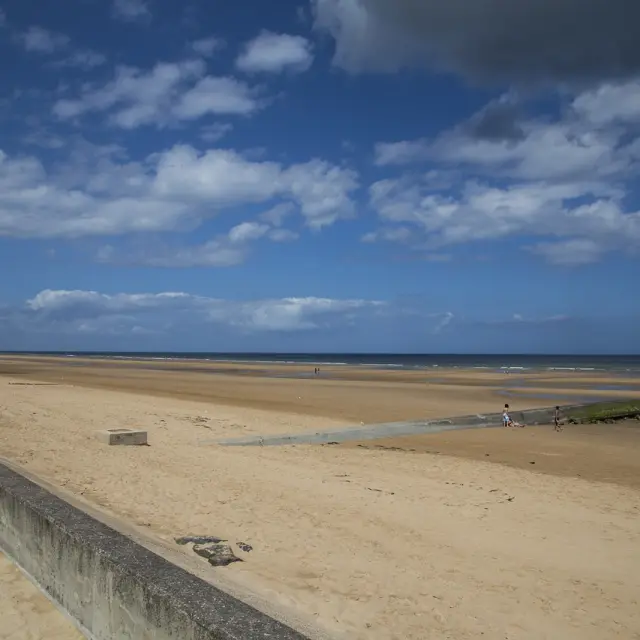 Sandstrand mit einigen Menschen in der Ferne und einem teilweise bewölkten Himmel