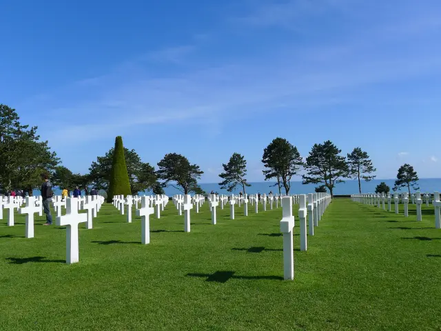Cimetière militaire avec des croix blanches alignées sur une pelouse verte en bord de mer