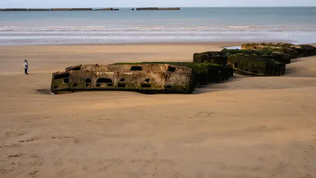 Reste de blockhaus sur la plage avec une personne à proximité à Arromanches