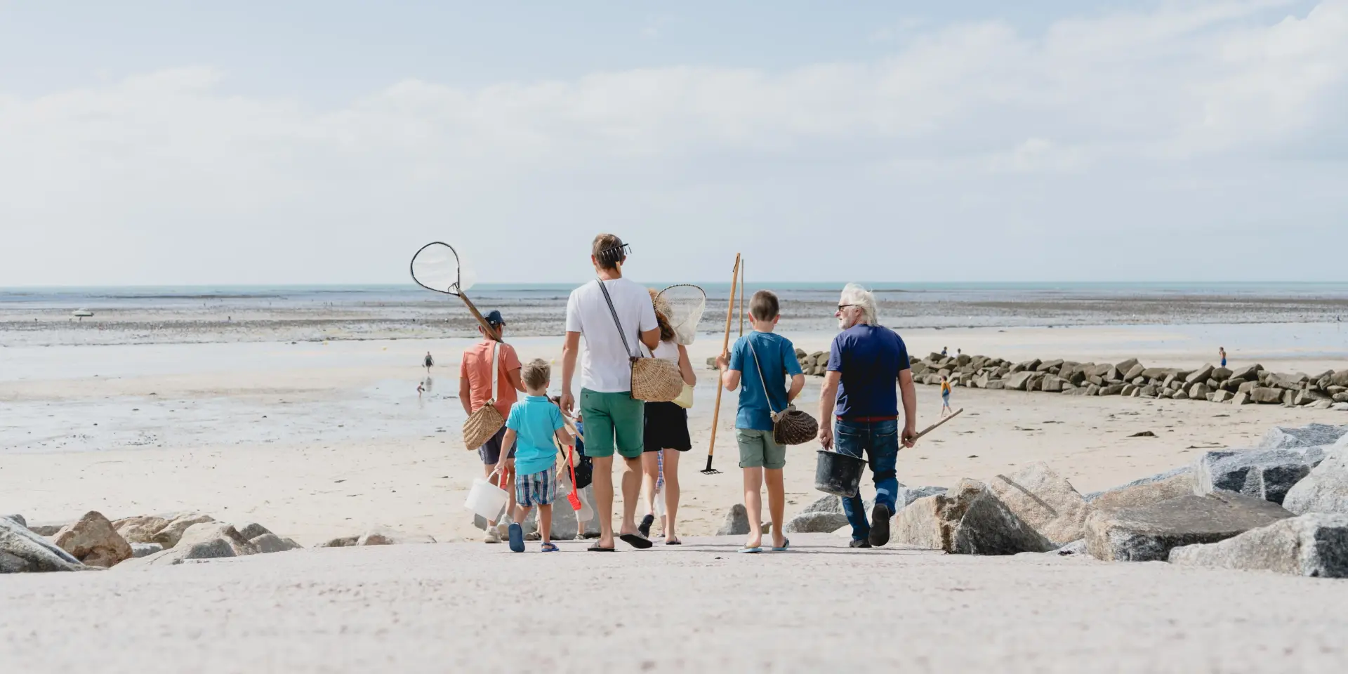 Une famille marchant sur une plage de sable avec des filets pour la pêche à pied à Agon COutainville