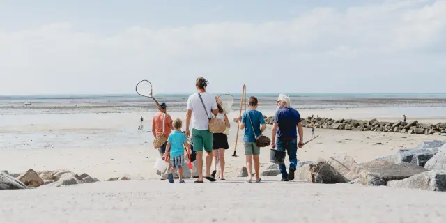 Une famille marchant sur une plage de sable avec des filets pour la pêche à pied à Agon COutainville