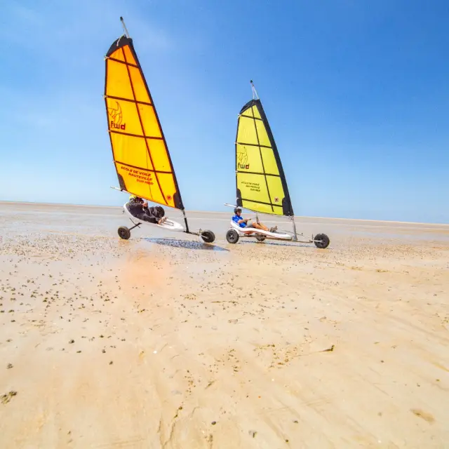 Two land sailors with yellow sails on a deserted beach