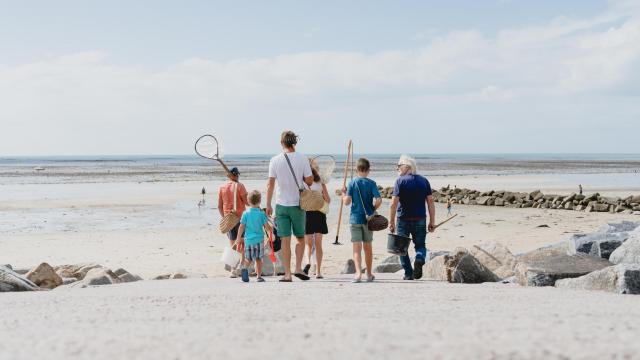 Une famille marchant sur une plage de sable avec des filets pour la pêche à pied à Agon COutainville