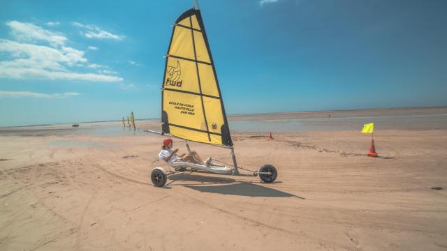 Person steering a small sailboat on a sandy beach