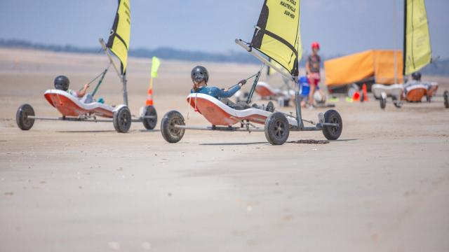 Two people driving land sail karts on a beach