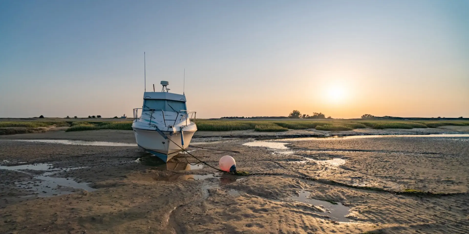 Ein weißes Boot gestrandet auf einem Sandstrand bei Sonnenuntergang