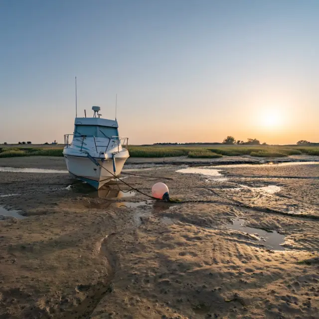 A white boat stranded on a sandy beach at sunset