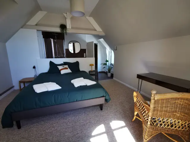 Chambre avec lit, chaise en osier et lumière naturelle à la Villégiature de Coutances