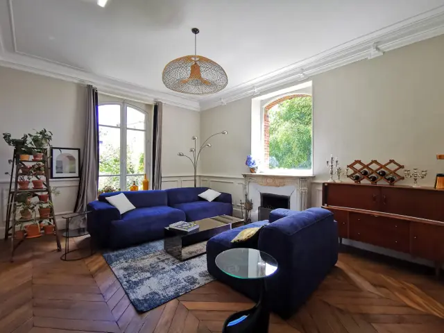 Salon avec canapé bleu, cheminée et grandes fenêtres à la Villégiature de Coutances