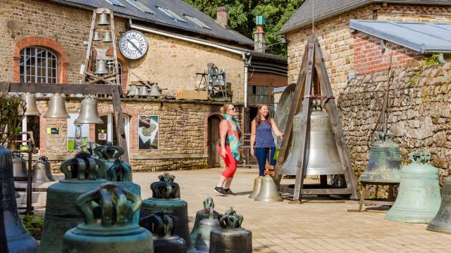Two people visiting a bell museum with many bells on display