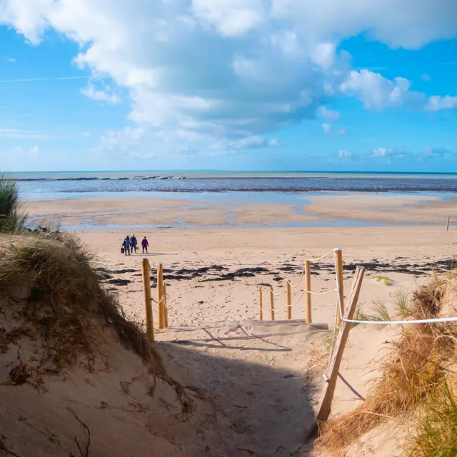Sandy beach with a few people in the distance and a blue sky with clouds