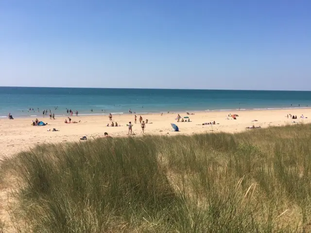 Sandstrand mit Menschen, die schwimmen und sich unter einem klaren blauen Himmel entspannen