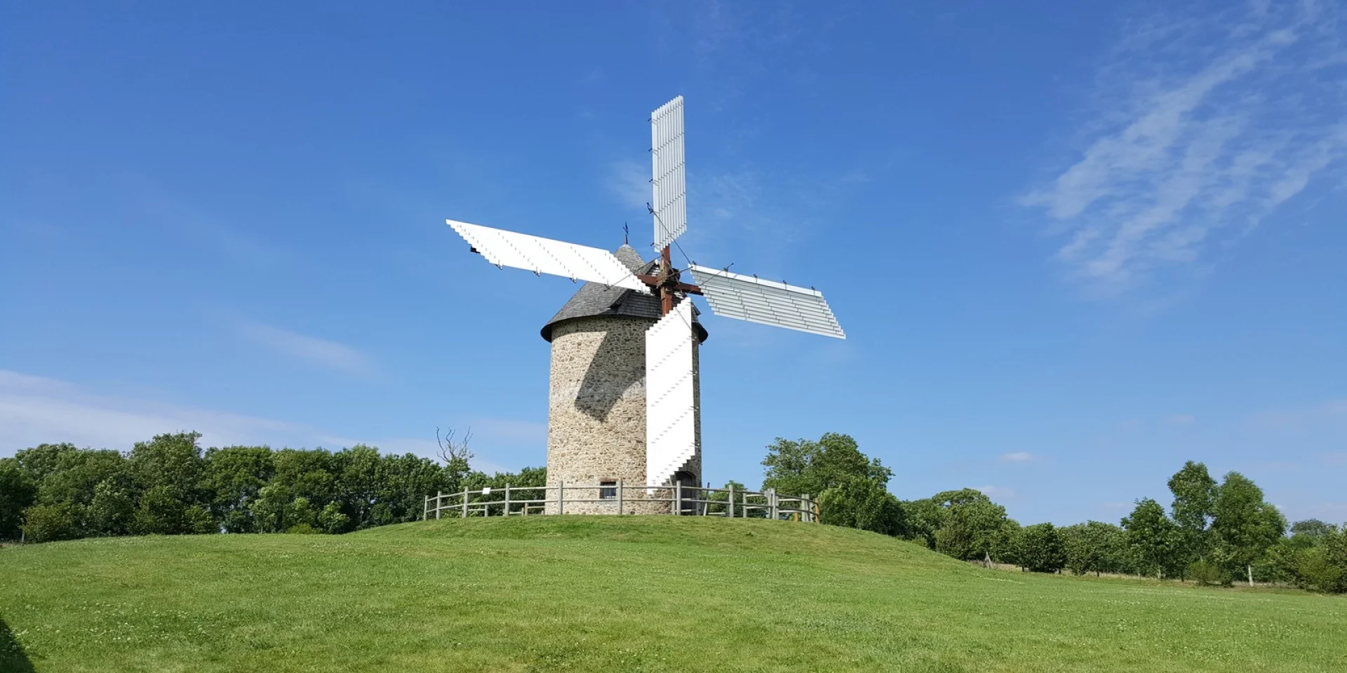 A white and gray windmill on a green hill
